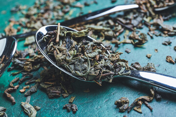 Spoons with dry green tea on color background