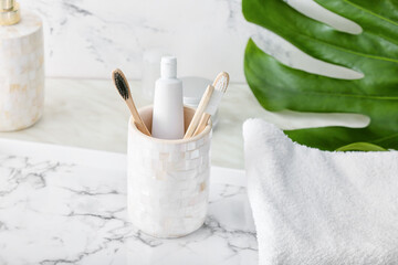 Holder with wooden toothbrushes and toothpaste on table in bathroom