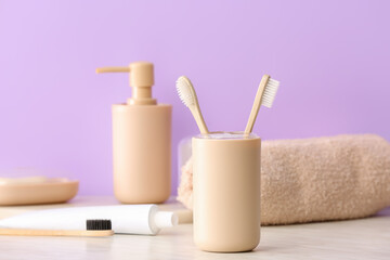 Holder with wooden toothbrushes and toothpaste on table in bathroom
