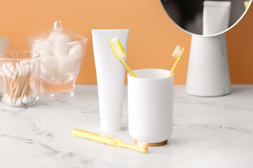 Holder with toothbrushes and toothpaste on table in bathroom