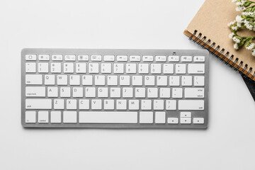 Computer keyboard, notebooks and flowers on light background