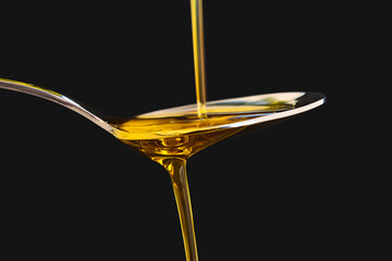 Olive oil liquid on a spoon over black background. Cooking
