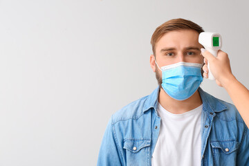 Man and hand with infrared thermometer on light background. Coronavirus epidemic