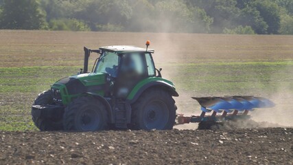 Farmer Ploughing Soil using Tractor with Mouldboard Plough on Sunny Day