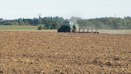 Fototapeta premium Farmer Ploughing Soil using Tractor with Mouldboard Plough on Sunny Day