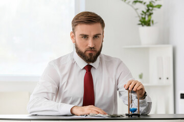 Businessman with hourglass and money at table in office