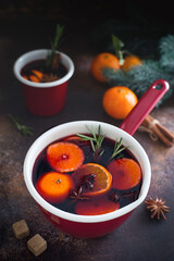Spicy aromatic mulled wine with tangerine and spices in a red enamel bowl, selective focus