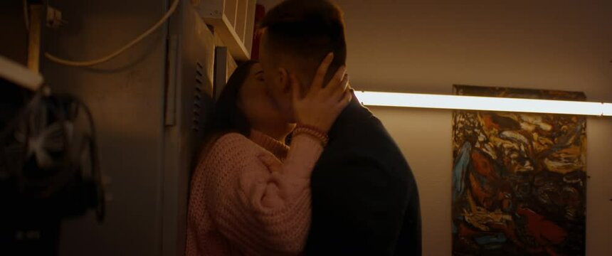 HANDHELD Teenagers kissing passionately inside a garage, having an intimate moment. Shot with 2x anamorphic lens