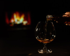 Close-up of a female hand with a glass of brandy on the background of the fireplace