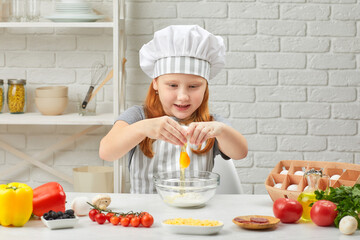 cute little girl in chef hat and an apron is breaking yellow egg into fresh dough in the kitchen. child cooking with dough