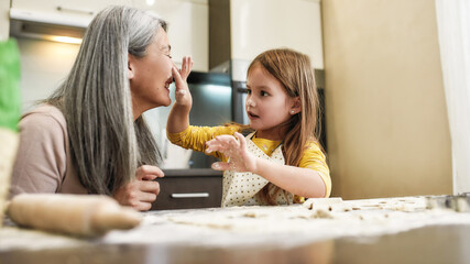 Little girl smearing laughing grandmother with flour at home