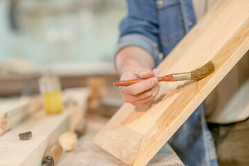 Craftsman applies varnish on wooden board with paintbrush in  carpentry workshop. Empty space for text