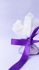 gift wrapped in white tissue paper and tied with purple satin ribbon on white background