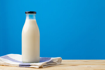 Glass bottle of milk on wooden table against blue background