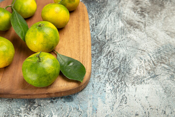 Half shot of fresh green mandarins with leaves on wooden cutting board on gray background