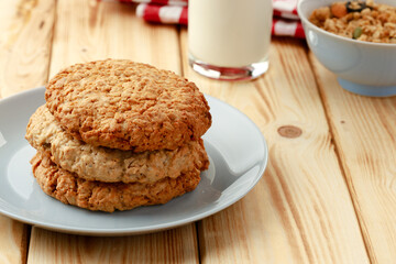 Oat cookies with oat flakes and cup of milk on wooden table
