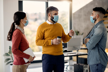 Businessman talking to his colleagues on a break while wearing face masks in the office.