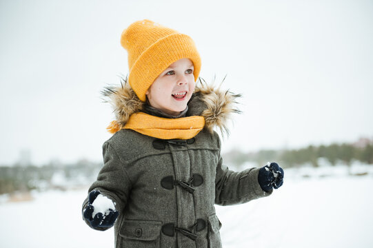 Cute a boy in warm yellow hat and gray overcoat walking in winter the forest.