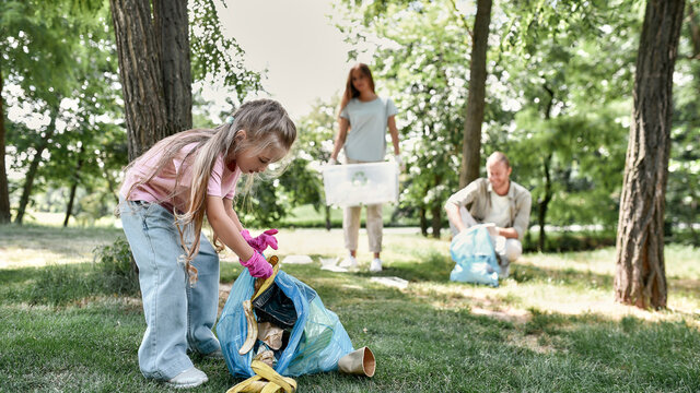 Clean up day with family. Cute little girl holding trash bag and collecting garbage while cleaning with parents in the park or forest