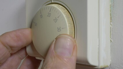 Closeup POV shot of a man’s fingers turning up the thermostat for an old domestic heating system, setting it to a little over 20 degrees celsius / centigrade.