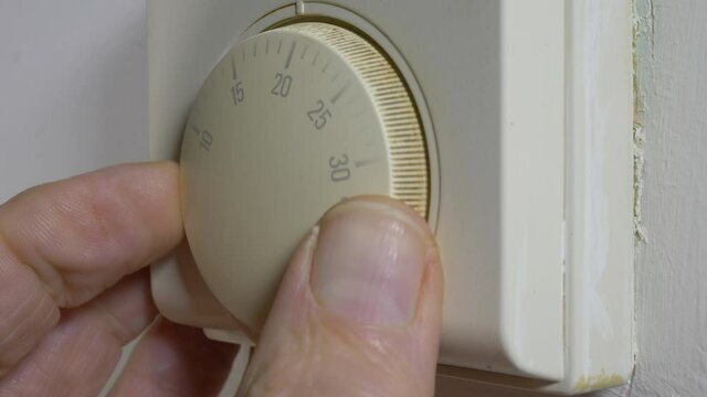 Closeup POV shot of a man&rsquo;s fingers turning up the thermostat for an old domestic heating system, setting it to a little over 20 degrees celsius / centigrade.