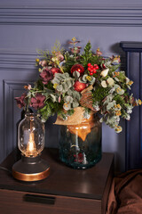 a beautiful New Year's bouquet in a transparent vase made of dark glass, next to it there is a small lamp with a decorative lamp with a filament