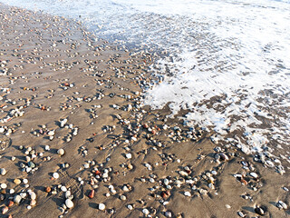 Sea water running on the sandy coastline with pebbles