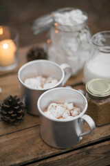 Hot cocoa with melted marshmallows and cinnamon on wooden table nearpot with milk.