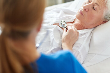 medicine, healthcare and old age concept - female doctor or nurse with stethoscope checking heartbeat or breath of senior woman at hospital