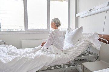 medicine, healthcare and people concept - lonely senior woman sitting in bed at hospital ward