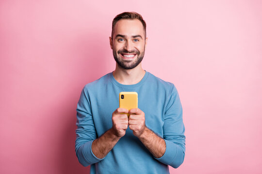 Photo of charming young man dressed blue sweater smiling typing modern device isolated pink color background