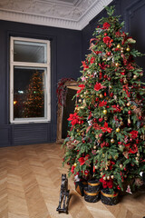 Fototapeta na wymiar a tall beautiful Christmas tree against the background of gray walls and a white window and ceiling with moldings. tree decorated with red balls and flowers. there are black and gold gift boxes under 
