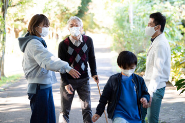 マスクをした若い親子と夫婦が仲良く公園で散歩をしている