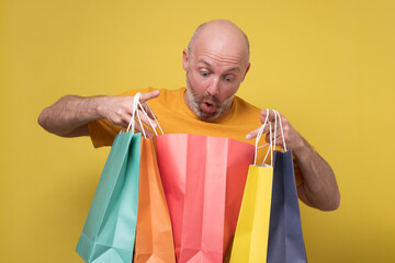 Mature hispanic man with beard holding shopping bags from mall. Studio shot on yellow wall.