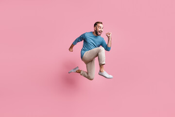 Fototapeta na wymiar Full length photo of hurry funky young guy wear blue pullover jumping running fast isolated pink color background