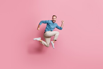 Full length photo of purposeful funny young man dressed blue sweater jumping high running isolated pink color background