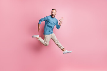 Fototapeta na wymiar Full length photo of handsome sweet young guy wear blue pullover jumping waving arm isolated pink color background