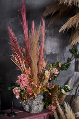 a beautiful bouquet with roses and dried flowers and pink pampas grass stands next to black tall...