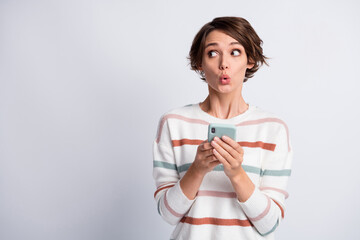 Photo of excited cute young lady wear striped sweater holding modern gadget looking empty space isolated grey color background