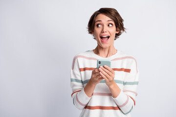 Photo of tricky excited young lady wear striped sweater holding modern gadget looking empty space isolated grey color background