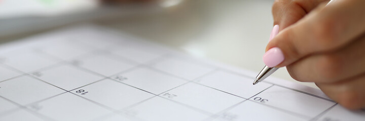 Woman's hand holds pen and marks calendar. Business calendar and task scheduling concept
