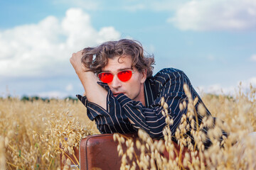 Tall handsome man with brown suitcase full of ears of oats laying at golden oat field.
