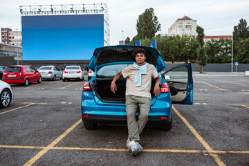 Young man sitting alone in open car trunk at autocinema