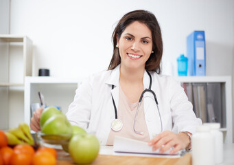 Beautiful smiling nutritionist looking at camera and showing healthy fruits