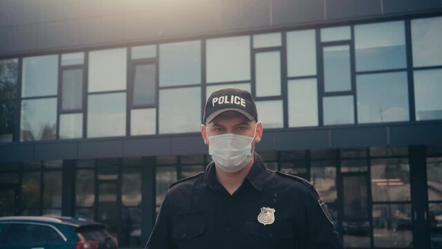 Policeman in uniform and medical mask looking at camera outdoors