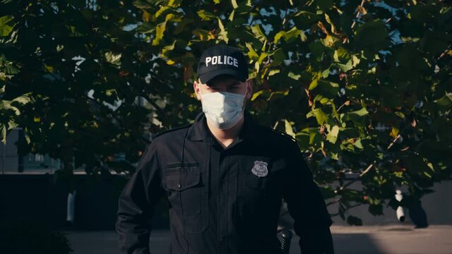 Policeman in medical mask standing near tree outdoors