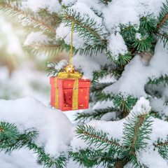 Close up Christmas decoration in the form of a gift on a spruce branch covered with natural snow. Winter christmas picture
