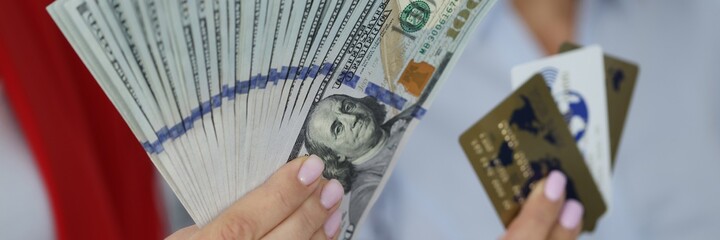 Female hands hold fan of one hundred American dollar bills and credit bank cards. Trading on the stock exchange and making money on the Internet concept