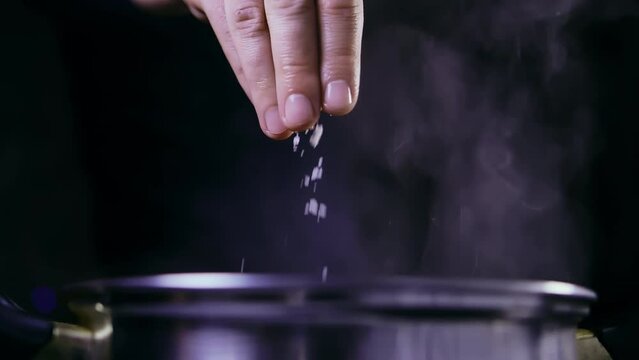 Man salt water boiling in a saucepan, dark background