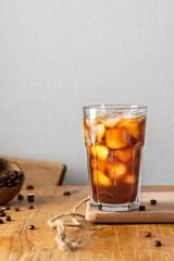 Cold refreshing iced coffee in a glass on a wooden board close-up, cocoa beans in coconut shell